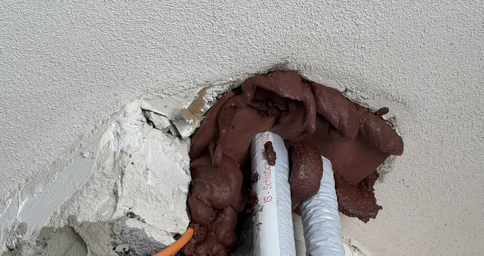 Wanddurchbruch mit Lüftungskanal und Abwasserleitung, ringsum mit Brandschutzsteinen verschlossen